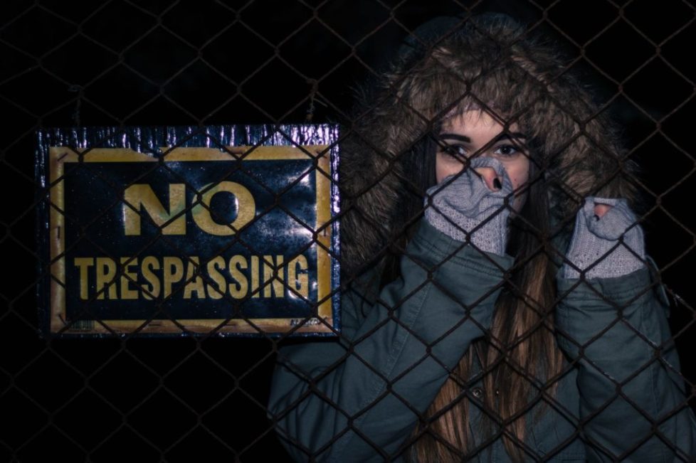 woman behind black chainlink fence with no trespassing signage